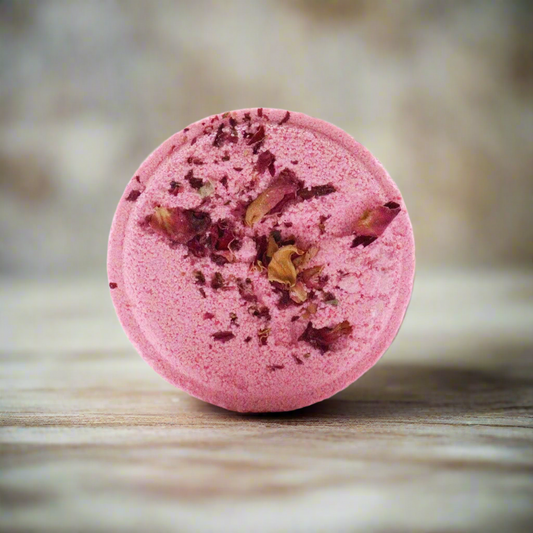 Pink bath bomb with rose petals on a wooden surface