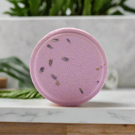 Pink bath bomb with specks on a marble surface with a blurred green plant background